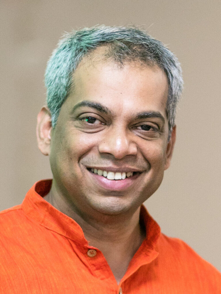 A man with blue hair and orange shirt smiling.